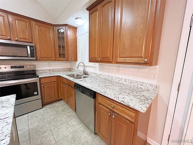 kitchen with light stone countertops, sink, stainless steel appliances, lofted ceiling, and decorative backsplash