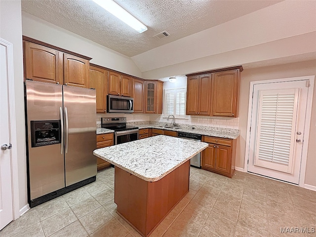 kitchen with sink, a textured ceiling, vaulted ceiling, a kitchen island, and appliances with stainless steel finishes