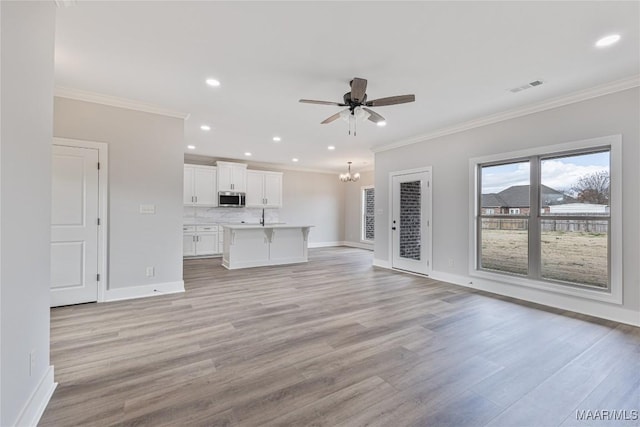 unfurnished living room with ceiling fan with notable chandelier, crown molding, and light hardwood / wood-style flooring