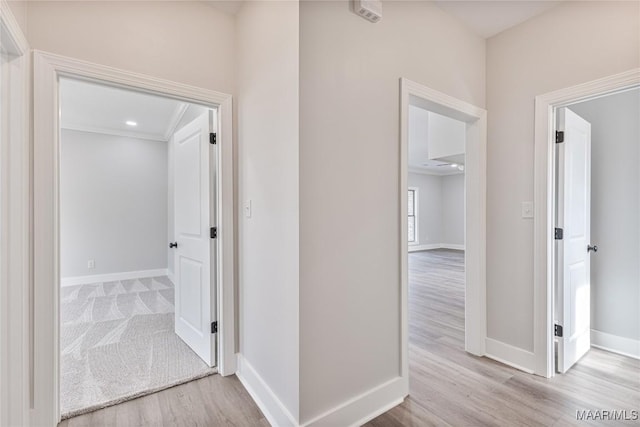 hallway with light wood-type flooring and crown molding