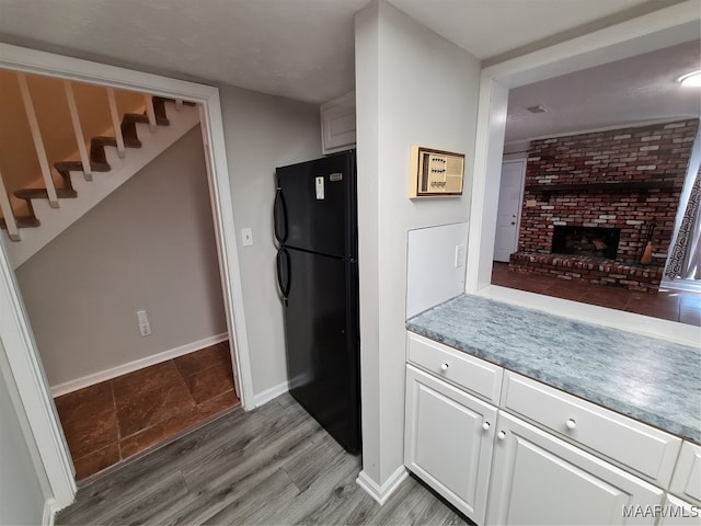 kitchen featuring brick wall, a brick fireplace, hardwood / wood-style floors, white cabinets, and black refrigerator