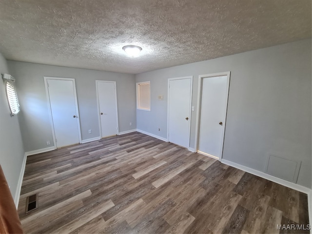 unfurnished bedroom with a textured ceiling, wood-type flooring, and multiple closets