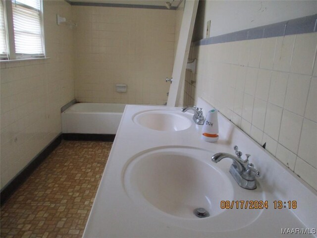 bathroom featuring tile walls, tile patterned floors, tiled shower / bath combo, and dual vanity