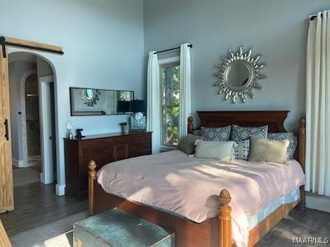 bedroom with arched walkways and dark wood-style flooring