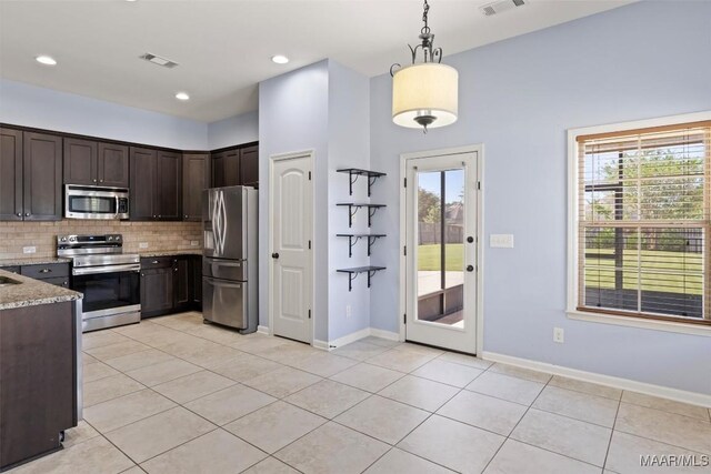 kitchen with tasteful backsplash, hanging light fixtures, appliances with stainless steel finishes, light stone countertops, and light tile patterned floors