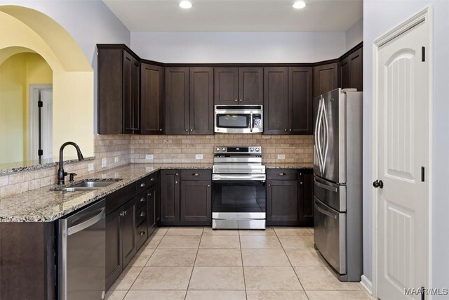 kitchen with backsplash, light stone counters, light tile patterned floors, sink, and stainless steel appliances