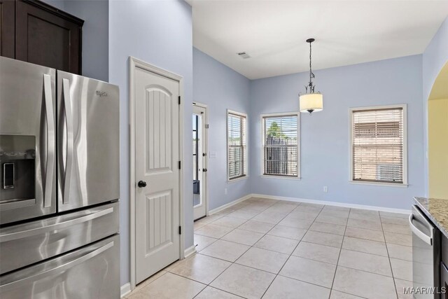 kitchen with decorative light fixtures, appliances with stainless steel finishes, dark brown cabinetry, light stone counters, and light tile patterned floors