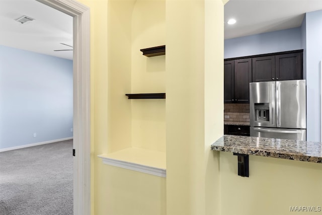 kitchen featuring decorative backsplash, stainless steel refrigerator with ice dispenser, ceiling fan, dark stone countertops, and light carpet