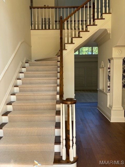 stairs with hardwood / wood-style floors, a towering ceiling, and decorative columns