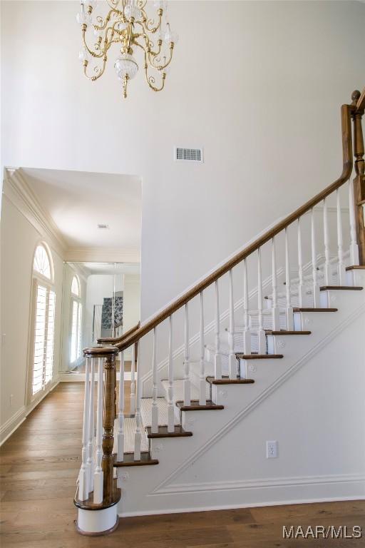 staircase with baseboards, wood finished floors, visible vents, and an inviting chandelier