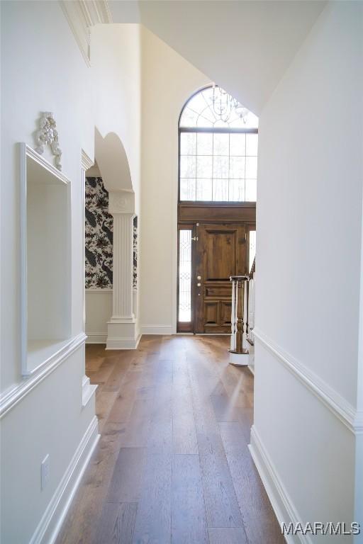 entrance foyer featuring decorative columns, wood finished floors, stairs, a high ceiling, and a notable chandelier