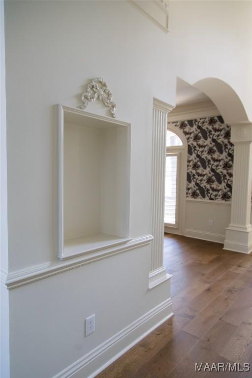 interior space featuring arched walkways, a wainscoted wall, ornate columns, and wood finished floors