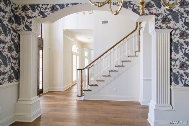 entryway with wallpapered walls, visible vents, arched walkways, wood finished floors, and ornate columns