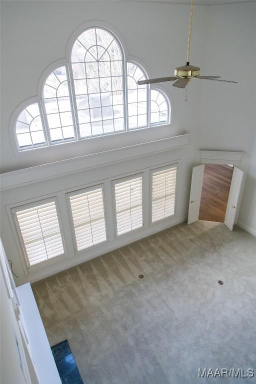 unfurnished living room with a towering ceiling, carpet, a ceiling fan, and a wealth of natural light