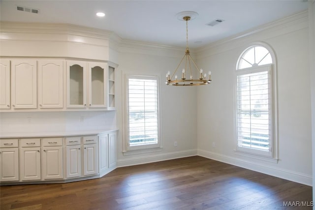 unfurnished dining area featuring dark wood-type flooring, visible vents, baseboards, an inviting chandelier, and crown molding