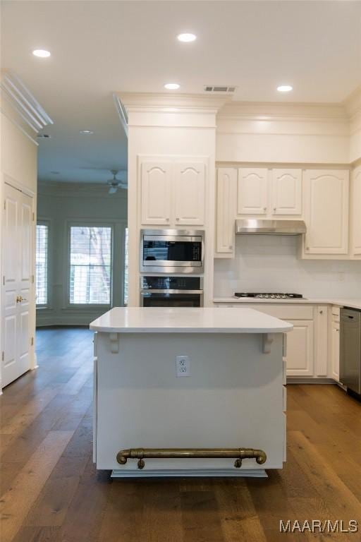 kitchen with crown molding, stainless steel appliances, dark wood-style floors, and under cabinet range hood