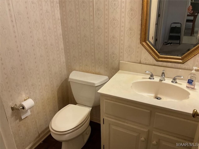 half bath featuring wallpapered walls, toilet, and vanity