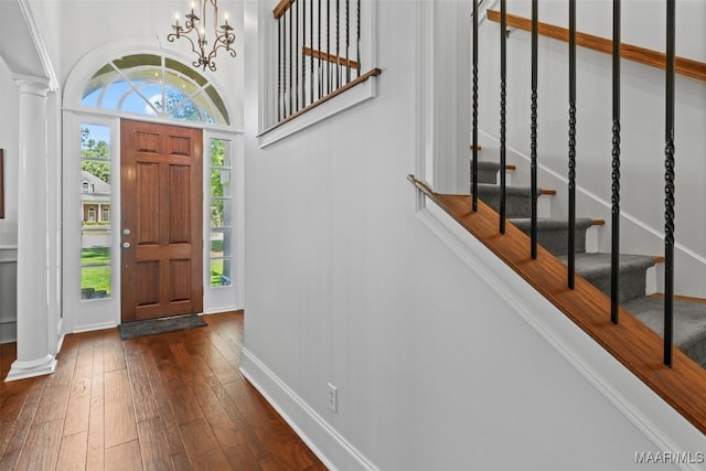 entrance foyer featuring decorative columns, dark wood-type flooring, and a notable chandelier