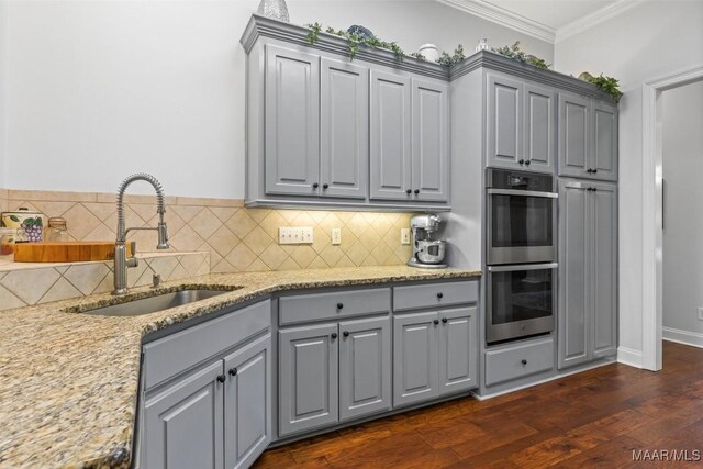 kitchen with gray cabinetry, dark hardwood / wood-style flooring, double oven, and light stone countertops