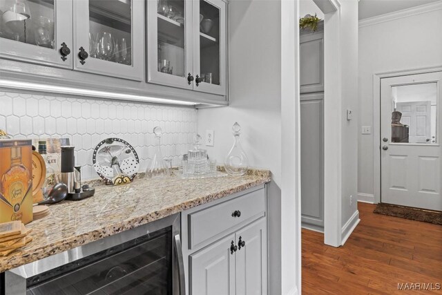 bar featuring dark wood-type flooring, tasteful backsplash, ornamental molding, light stone countertops, and wine cooler