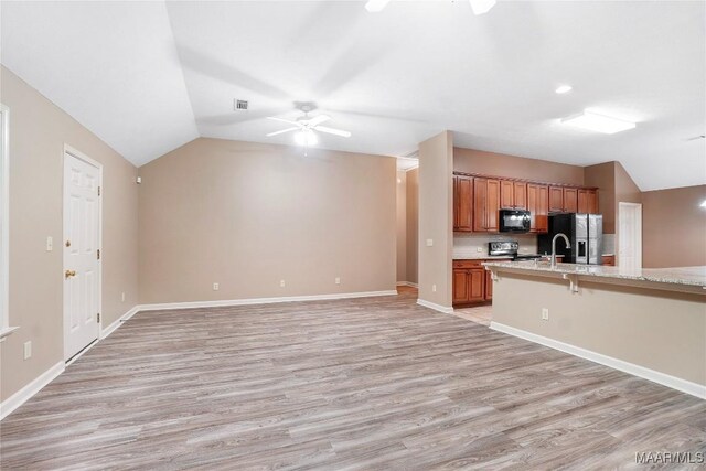 kitchen with ceiling fan, light wood-type flooring, a kitchen breakfast bar, appliances with stainless steel finishes, and lofted ceiling