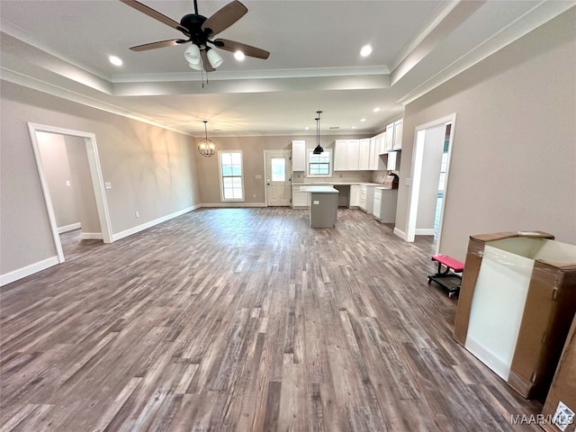 unfurnished living room featuring ornamental molding, ceiling fan with notable chandelier, wood-type flooring, and a tray ceiling