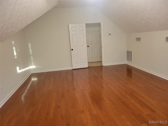 additional living space with dark hardwood / wood-style flooring, lofted ceiling, and a textured ceiling