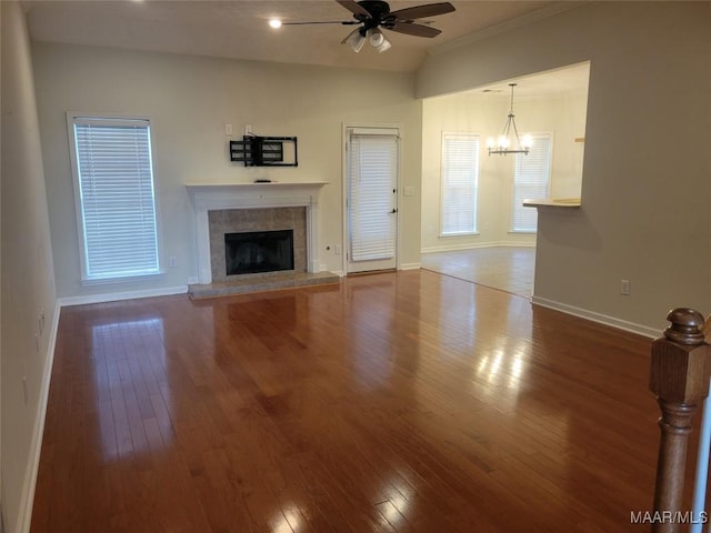 unfurnished living room with ornamental molding, ceiling fan with notable chandelier, hardwood / wood-style flooring, lofted ceiling, and a tiled fireplace