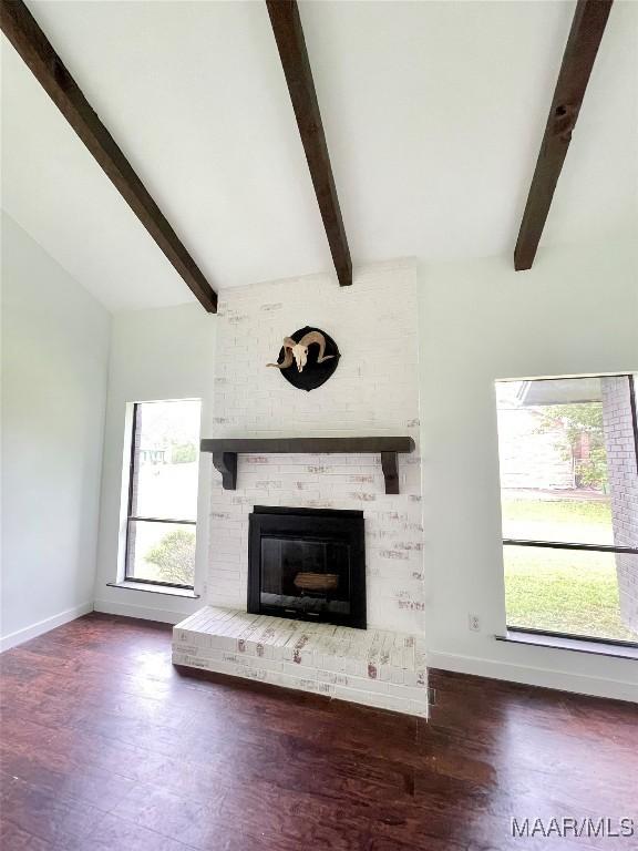 unfurnished living room with lofted ceiling with beams, a brick fireplace, baseboards, and dark wood-type flooring