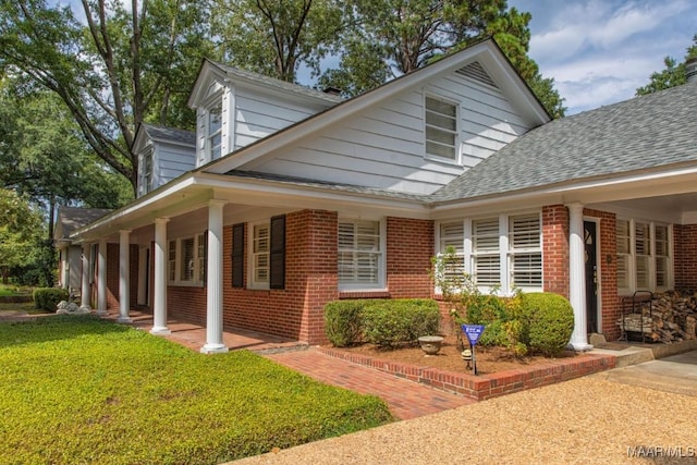 view of side of property featuring a shingled roof, brick siding, a yard, and a porch