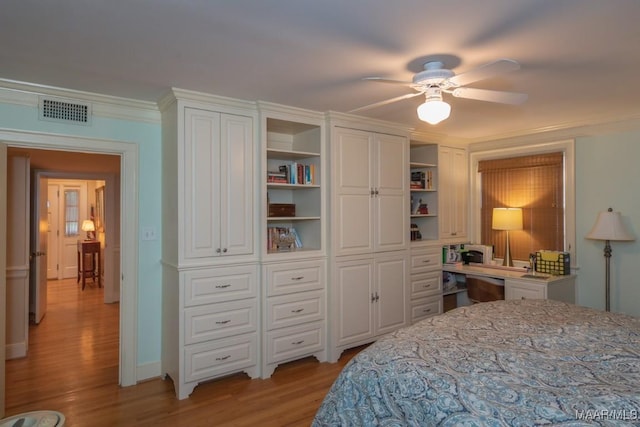 bedroom with visible vents, light wood-style flooring, ceiling fan, ornamental molding, and built in desk