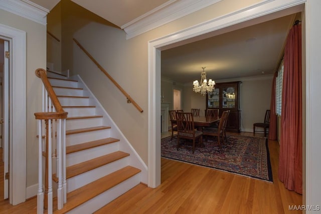 staircase with ornamental molding, wood finished floors, and an inviting chandelier