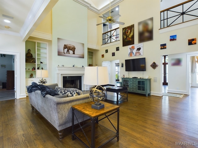 living room featuring built in shelves, ornamental molding, ceiling fan, and dark wood-type flooring