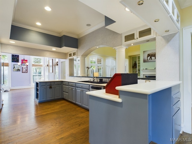 kitchen with kitchen peninsula, ornate columns, hardwood / wood-style flooring, ornamental molding, and sink