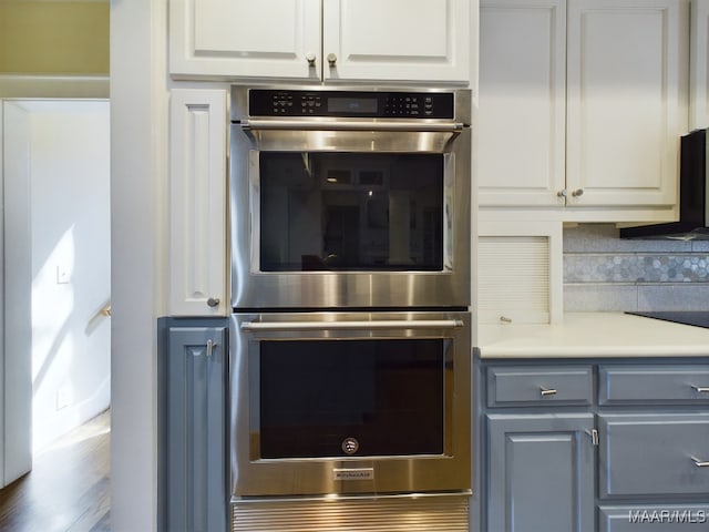 kitchen featuring stainless steel double oven, dark wood-type flooring, and white cabinetry