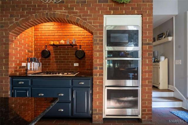 bar with dark stone counters, multiple ovens, blue cabinets, and brick wall