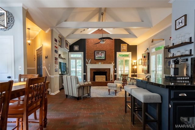 living room featuring ceiling fan, plenty of natural light, a brick fireplace, and lofted ceiling with beams