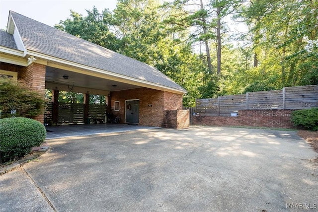 view of home's exterior featuring brick siding, a shingled roof, fence, a carport, and driveway