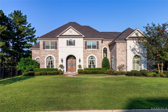 view of front of property with french doors, brick siding, roof with shingles, fence, and a front lawn