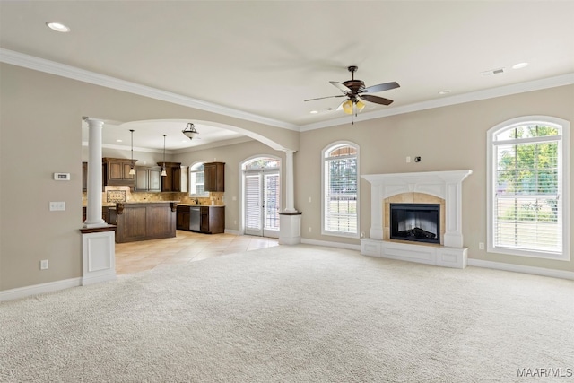 unfurnished living room with light colored carpet, decorative columns, crown molding, and ceiling fan