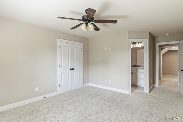 unfurnished bedroom with a closet, light colored carpet, ensuite bathroom, and ceiling fan