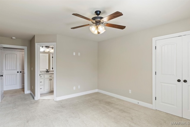 unfurnished bedroom featuring ceiling fan, light carpet, a closet, sink, and connected bathroom