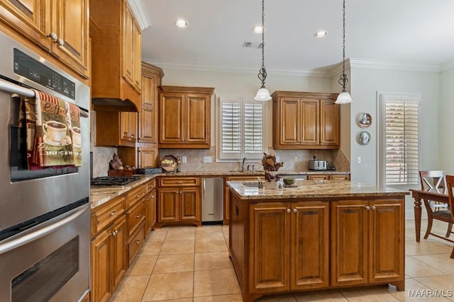 kitchen featuring double oven, a sink, gas stovetop, brown cabinetry, and an island with sink