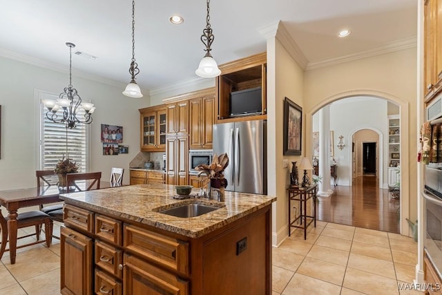 kitchen featuring stainless steel appliances, a kitchen island with sink, brown cabinets, and arched walkways