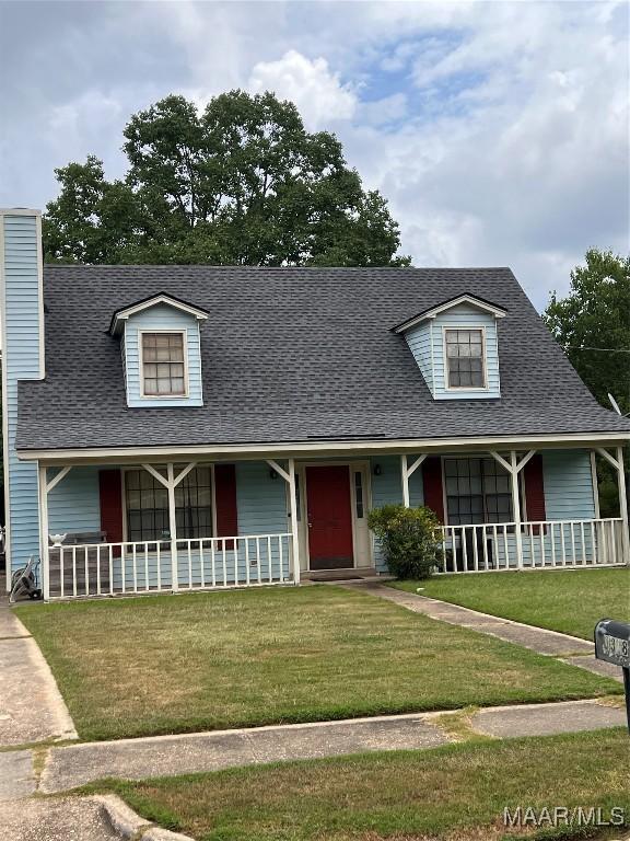 view of front of home with a chimney, roof with shingles, covered porch, and a front yard