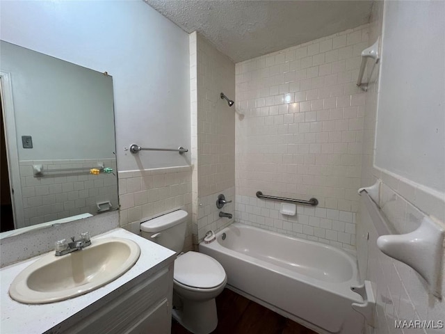 full bathroom with toilet, tiled shower / bath, tile walls, a textured ceiling, and vanity