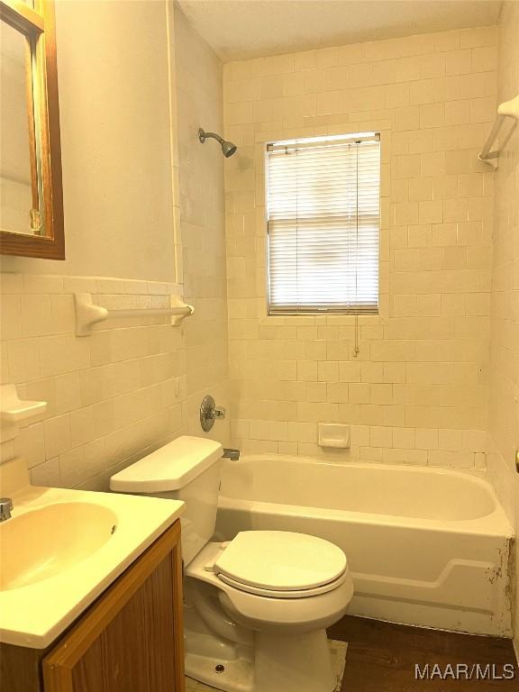 full bathroom with vanity, tiled shower / bath, tile walls, and toilet