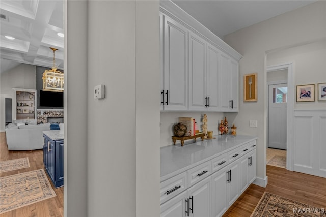 interior space with coffered ceiling, white cabinetry, beamed ceiling, and light hardwood / wood-style floors