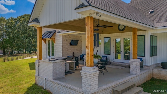 deck featuring ceiling fan, a patio area, french doors, a lawn, and exterior kitchen