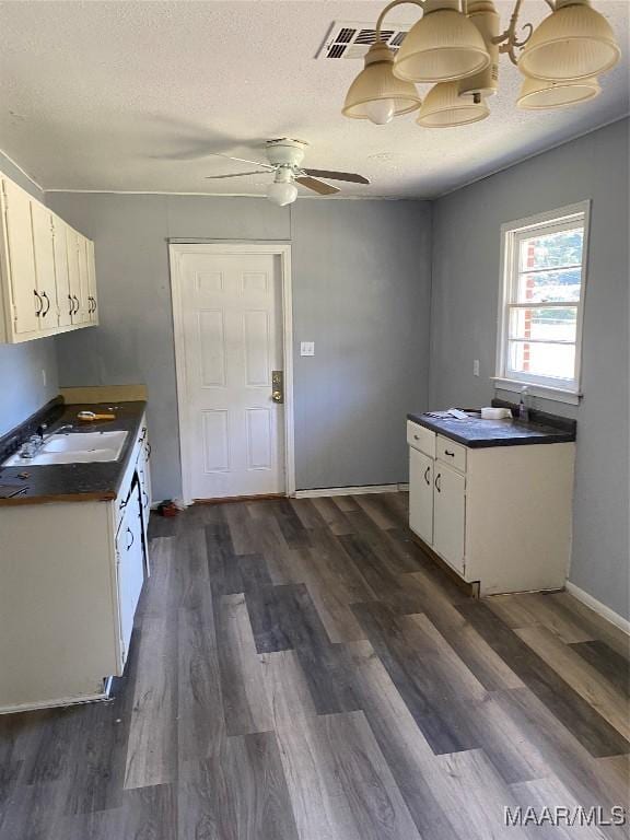 kitchen featuring a textured ceiling, dark wood-style flooring, a sink, white cabinets, and dark countertops